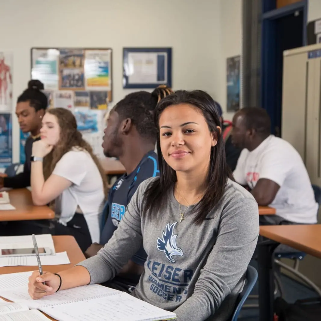 Smiling Keiser University student taking notes in a classroom
